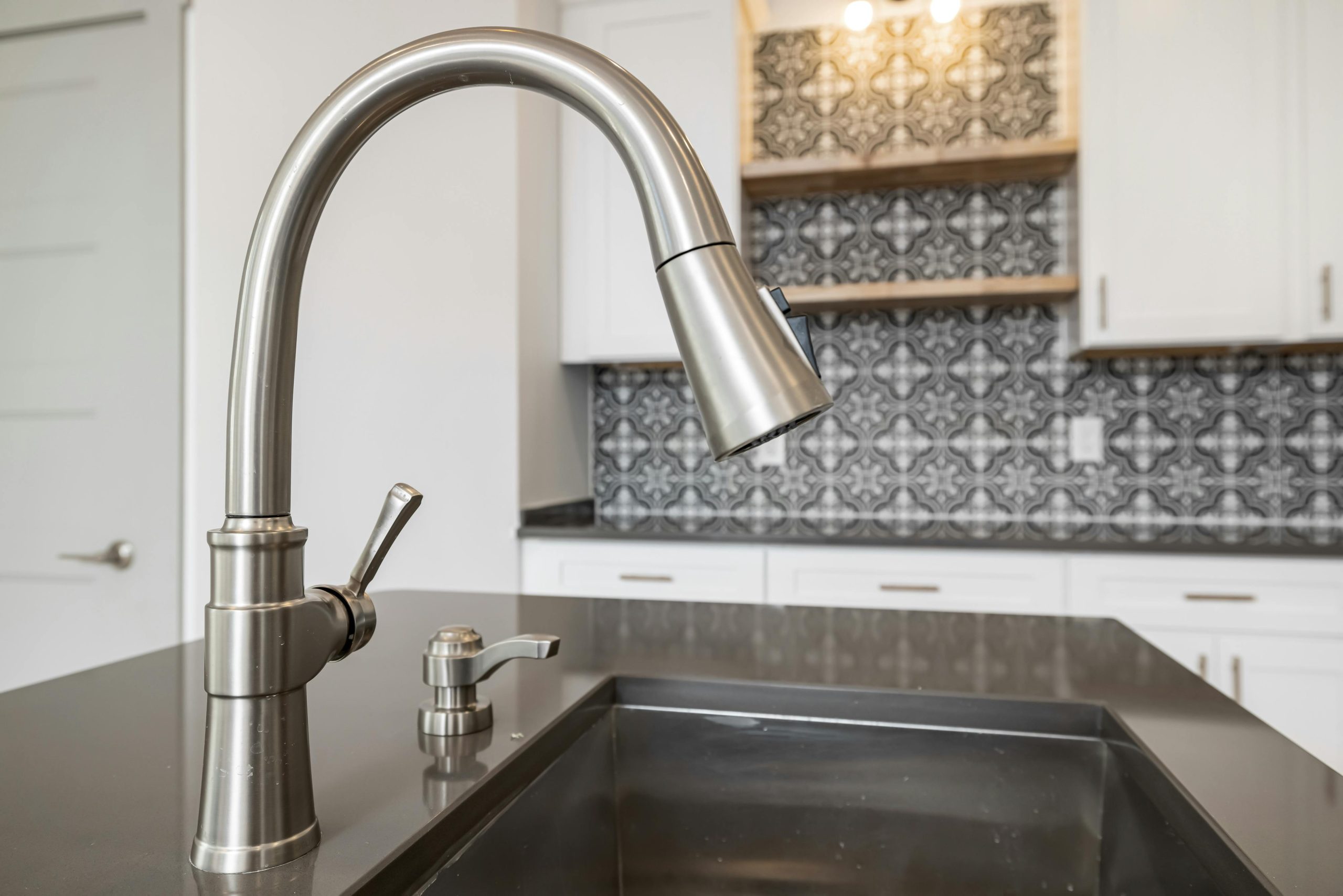 Close-up view of a modern stainless steel kitchen faucet with sleek design against tiled backsplash.