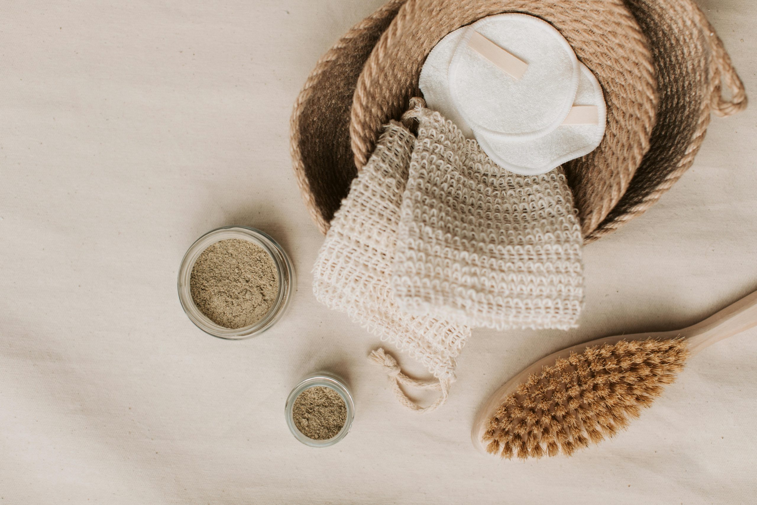 Flat lay of natural eco-friendly bathroom accessories including brush, scrubs, and reusable pads.